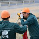two surveyors in hard hats using measuring equipment