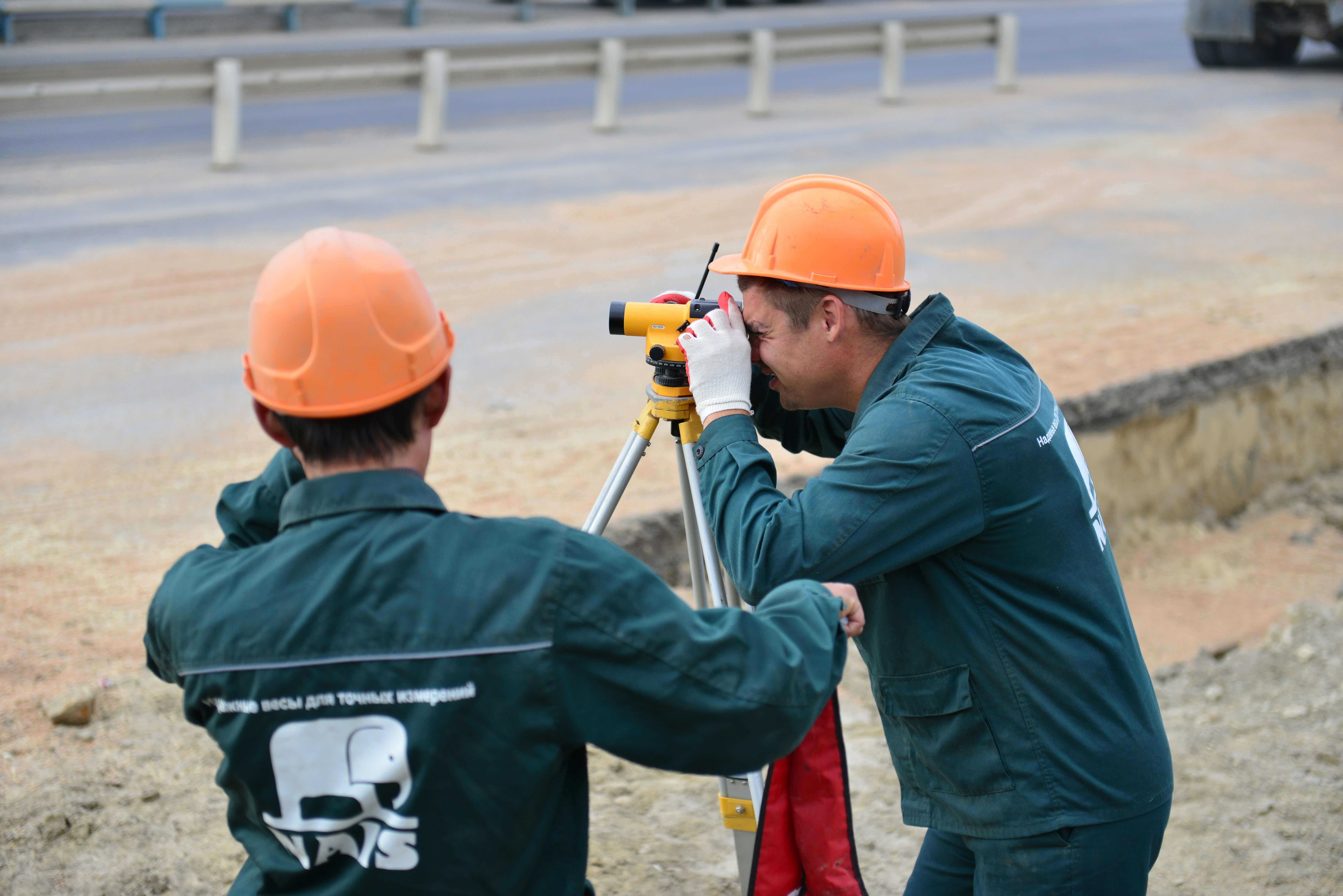 two surveyors in hard hats using measuring equipment