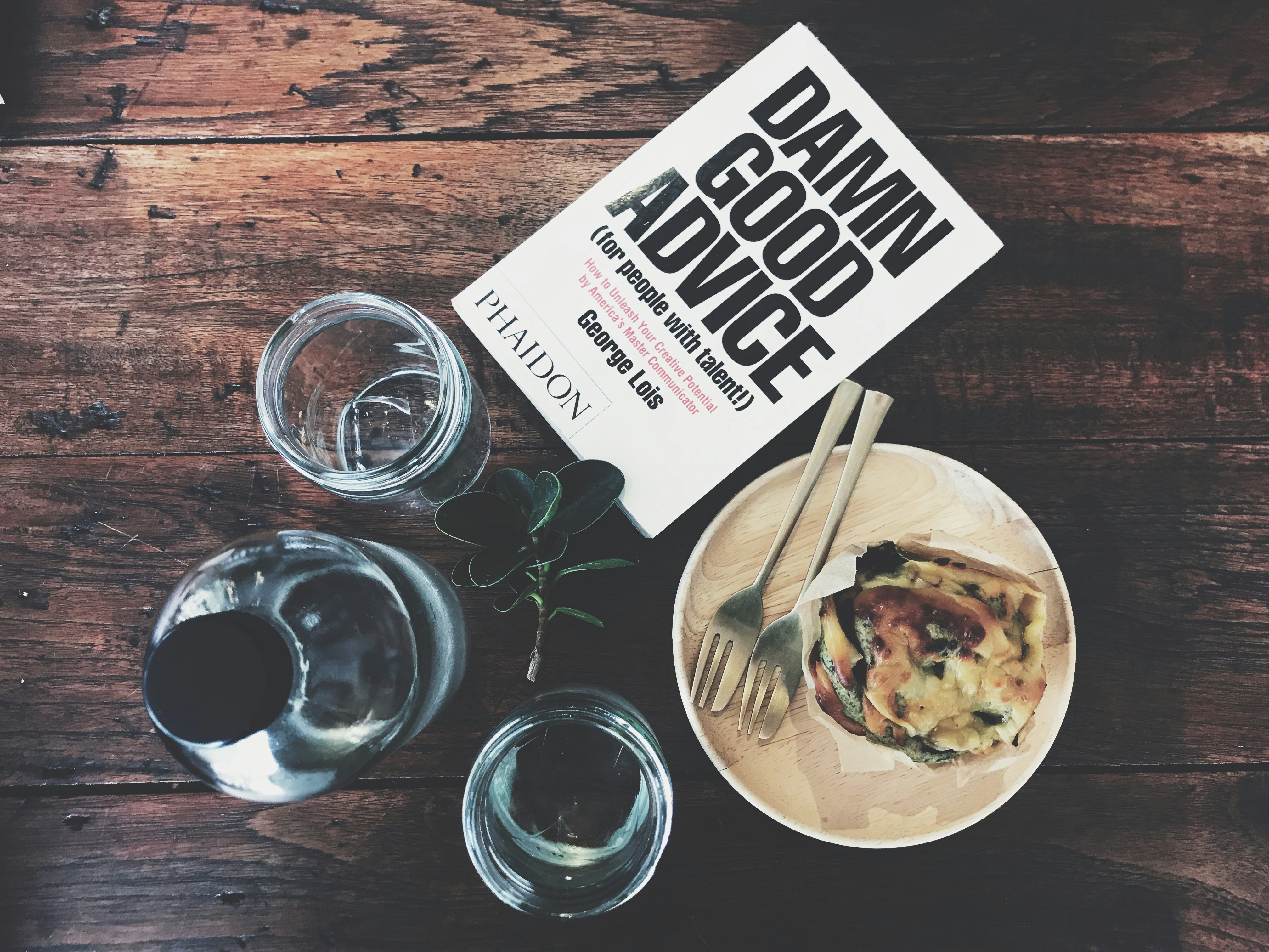 A book, cup and drinking glasses on a wooden table