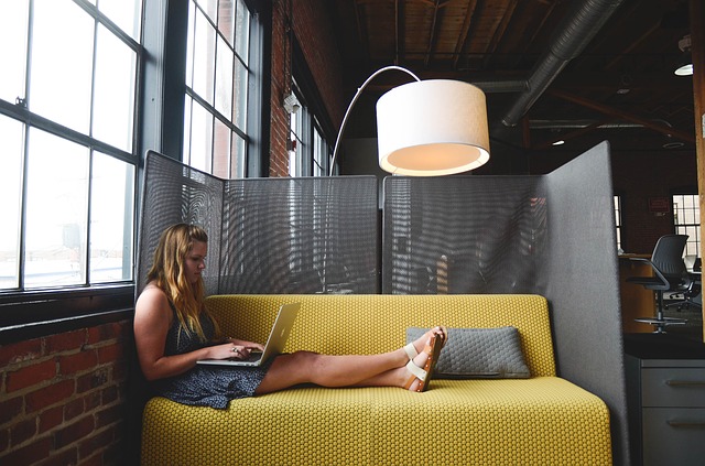 An entrepreneurial woman, lying on a sofa and working intently on her Apple Mac. 
