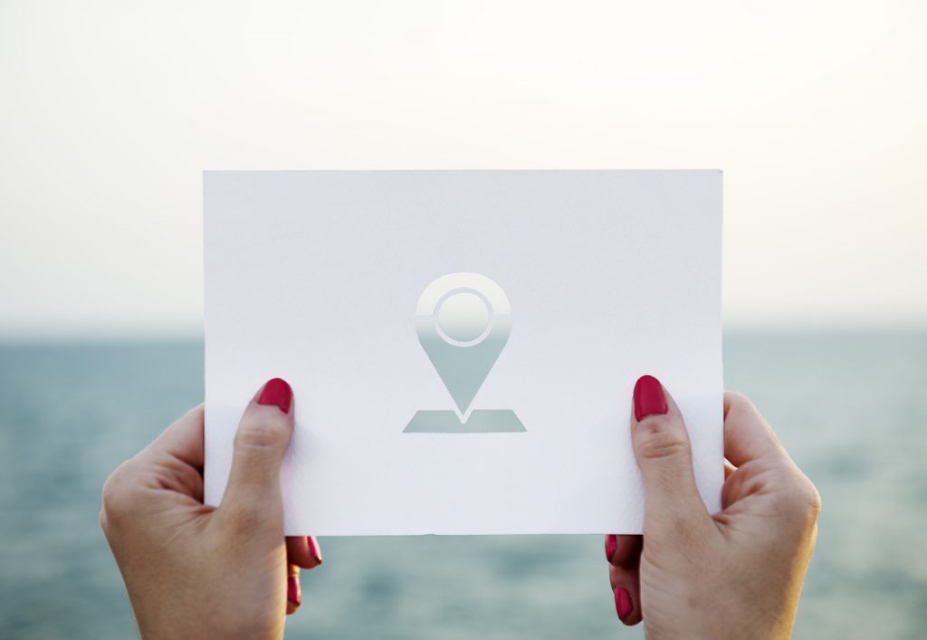 A woman holding a white card, adorning a GPS logo, against a beach backdrop. 