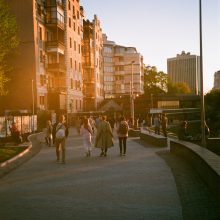 people walking by city apartments with sunshine on the buildings