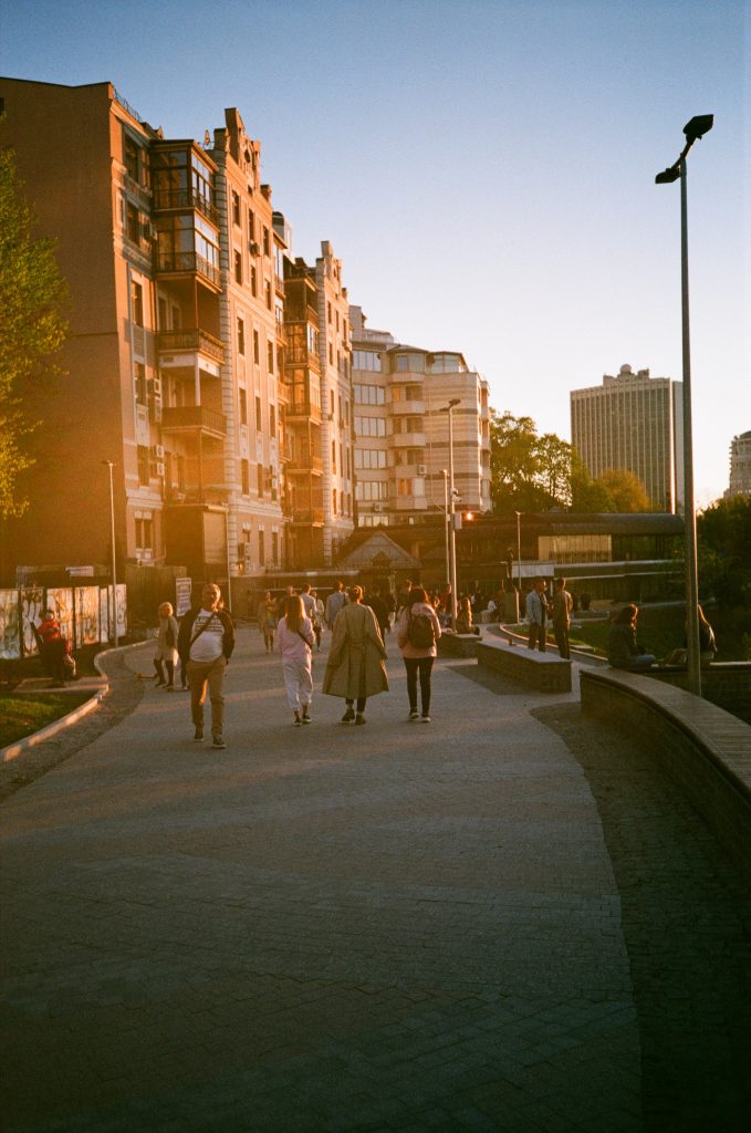 people walking by city apartments with sunshine on the buildings