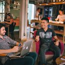 A group of people sitting in chairs with laptops and a cafe in the background.