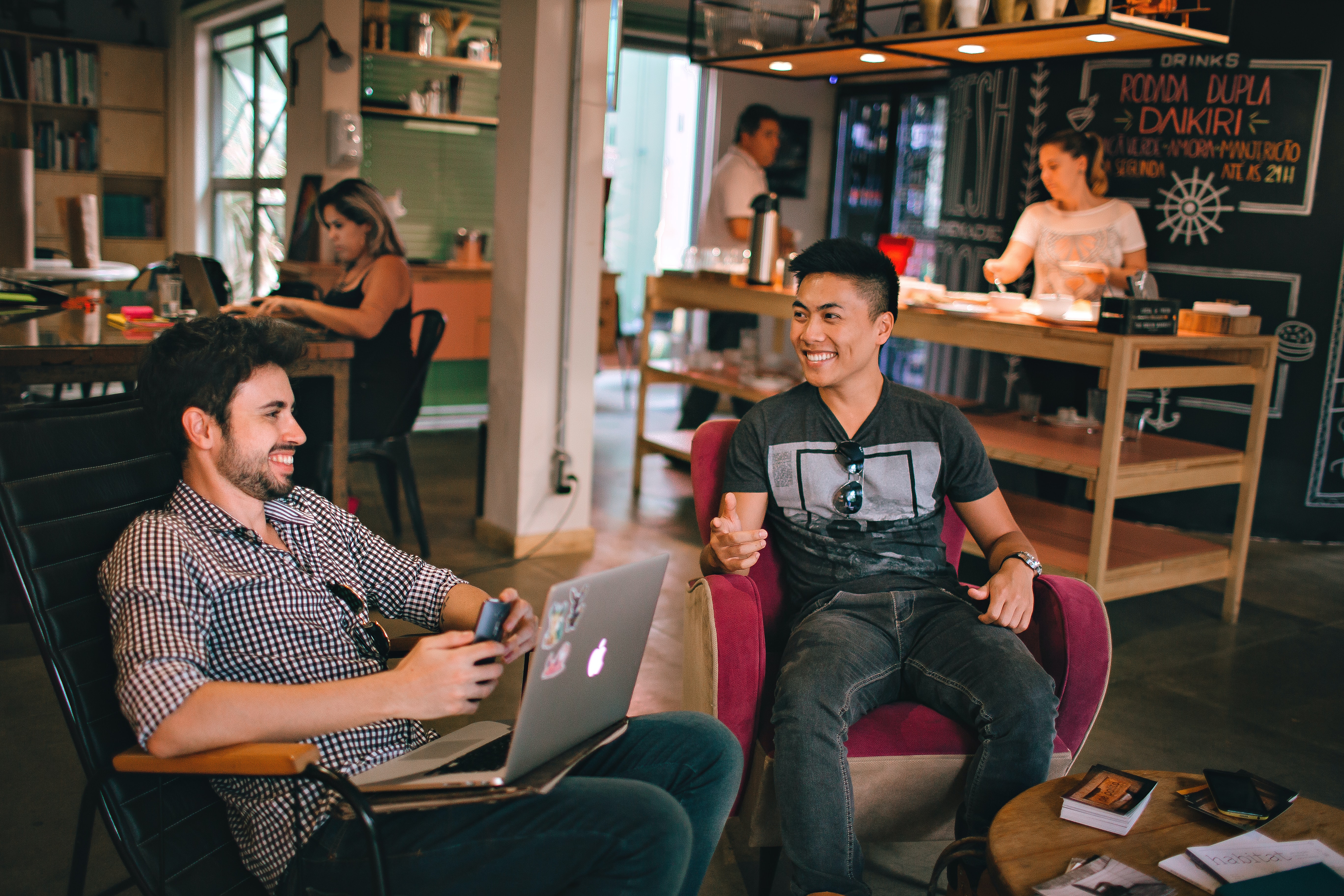 A group of people sitting in chairs with laptops and a cafe in the background.