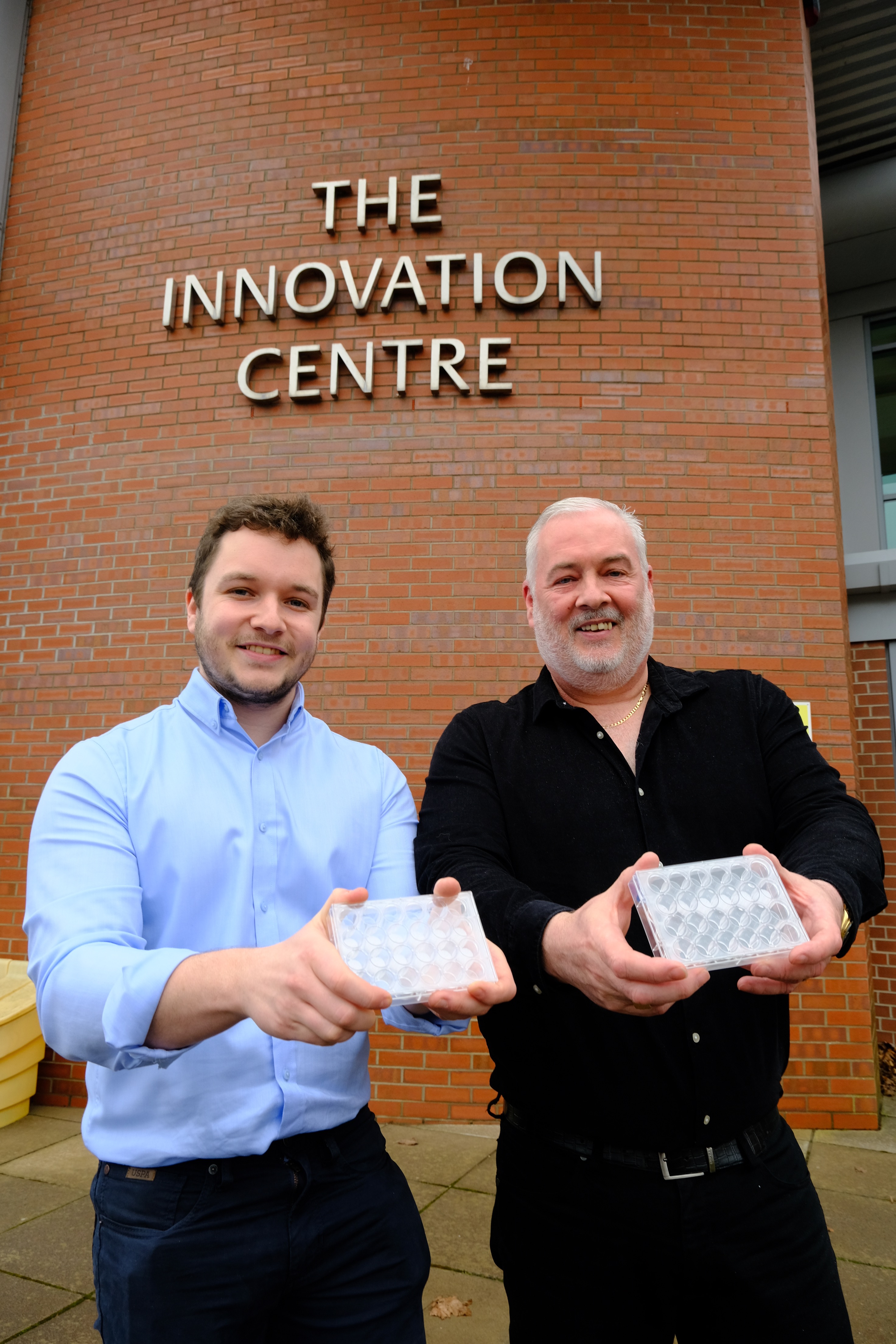 two white men in front of building holding lab equipment