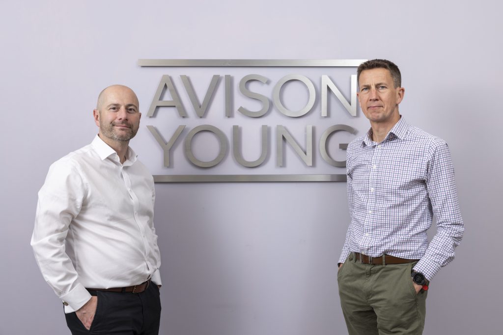 two men in front of an Avison Young sign 