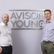 two men in front of an Avison Young sign