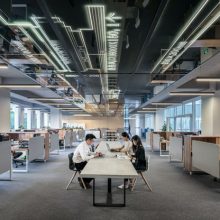 three people sat at a long desk in the middle of an office room