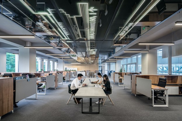 three people sat at a long desk in the middle of an office room 