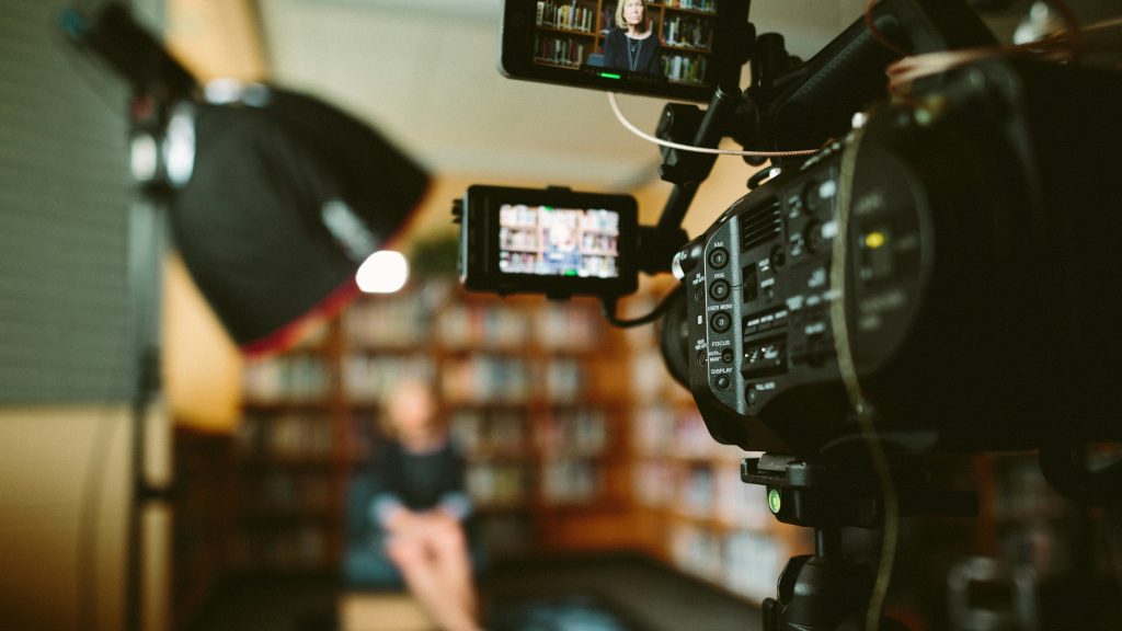 camera aimed at woman sat on chair in front of bookcase