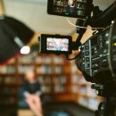 camera aimed at woman sat on chair in front of bookcase