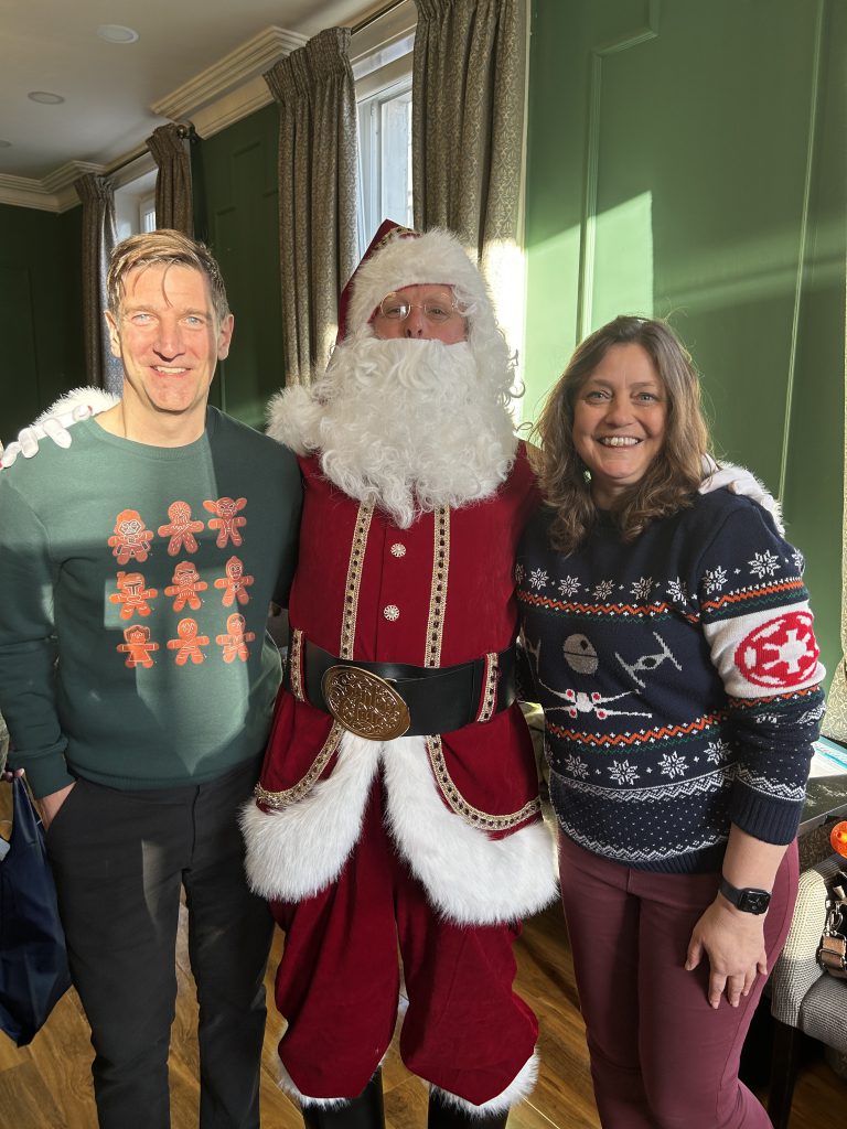 A mand and a woman in Christmas jumpers with Santa